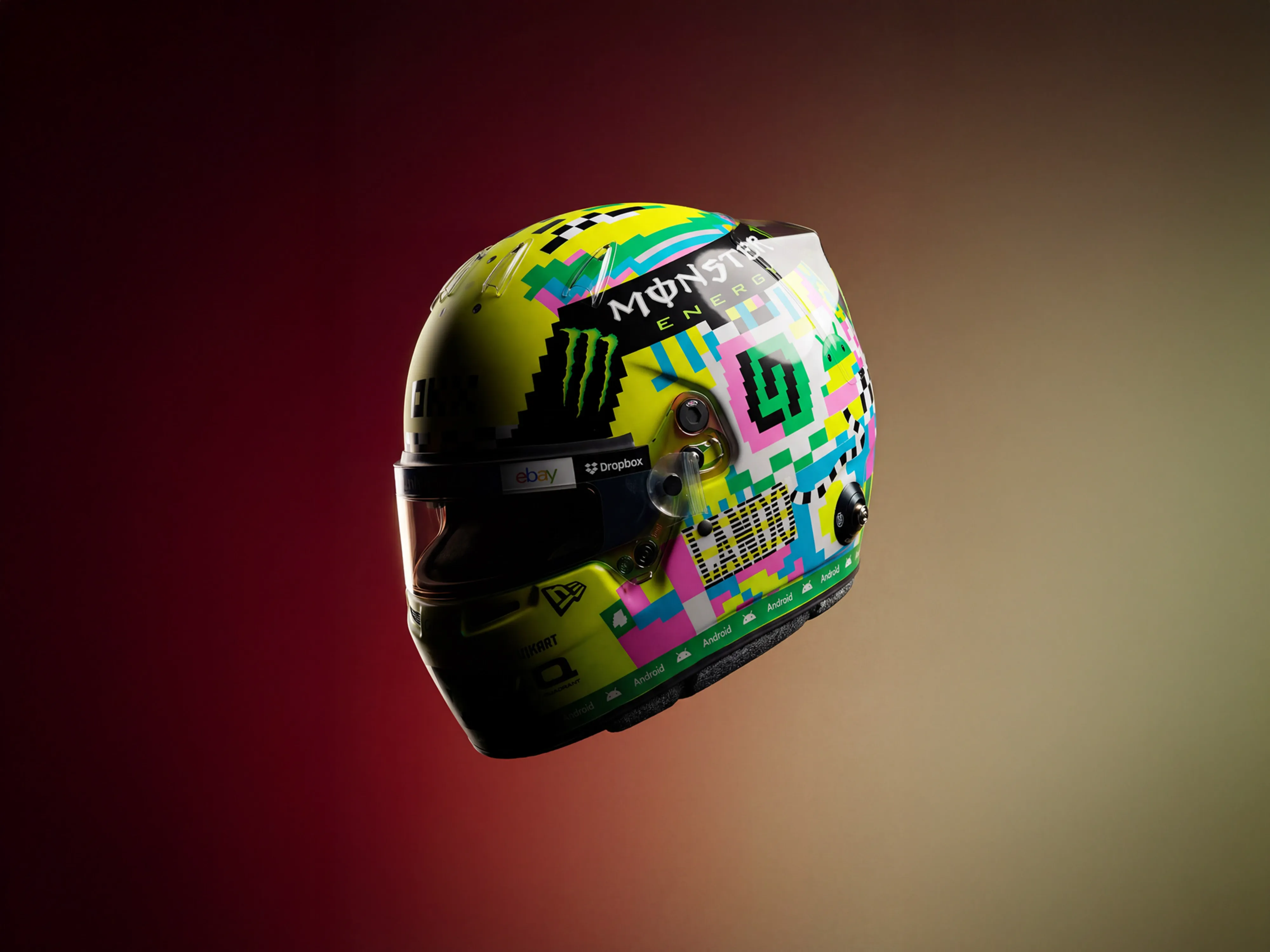 Vibrantly patterned racing helmet with colorful pixel designs, featuring logos against a gradient background.