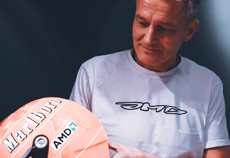 A person wearing a white T-shirt with a logo, looking at a racing helmet featuring logos.