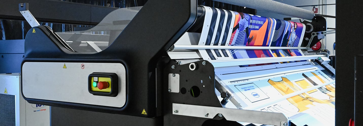 The Caron Cradle feeder feeding uncut rolls of textiles to a Summa laser cutter .