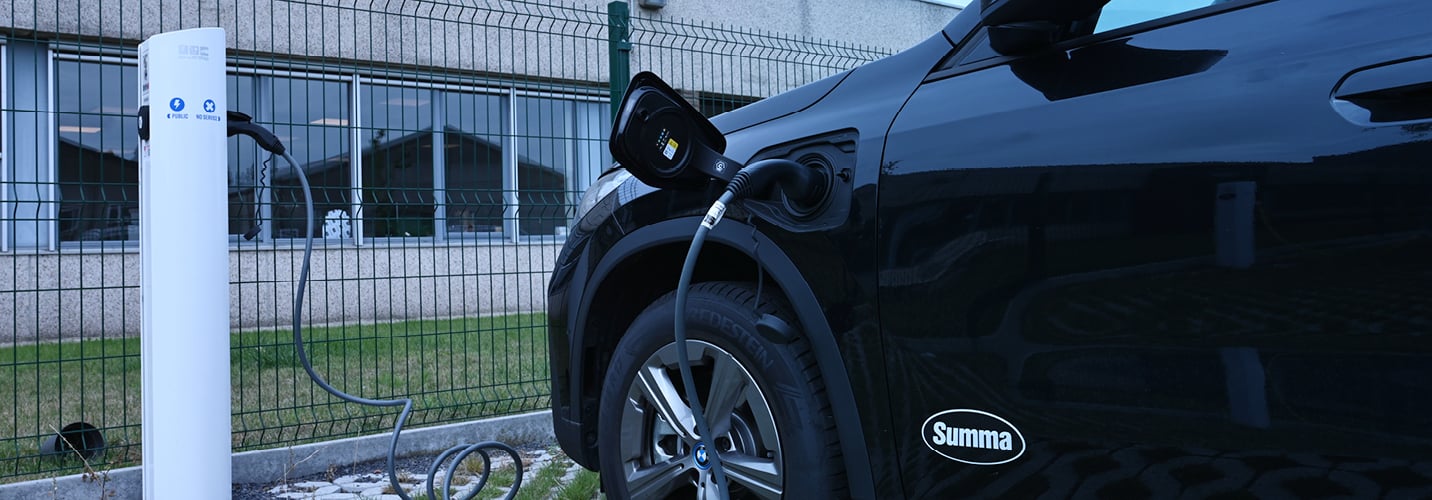An electric car is charging at a designated station in the Summa parking lot, highlighting the company's commitment to sustainable transportation.