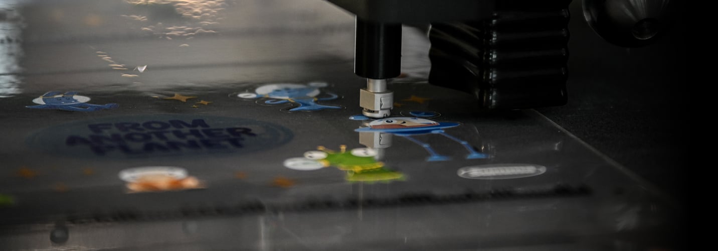 The tangential knife of a flatbed cutter is precisely cutting out small alien-shaped stickers.